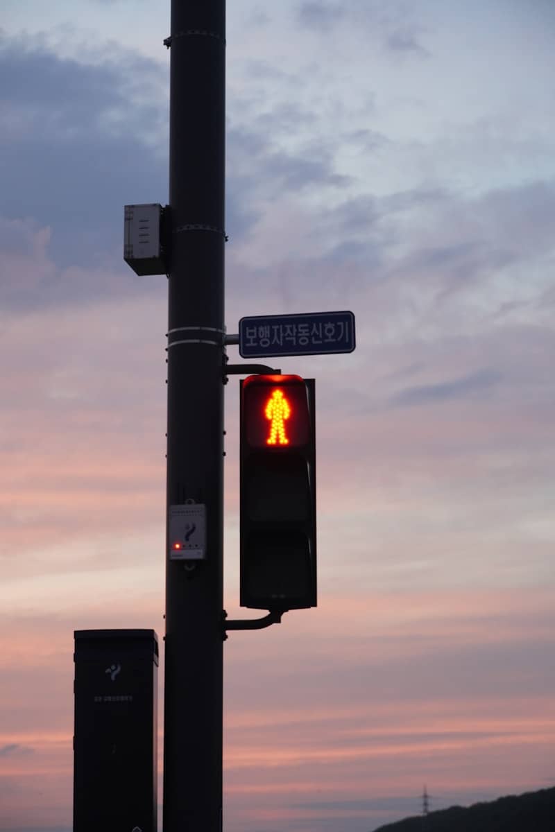 Red pedestrian signal on a pole against a sunset sky.