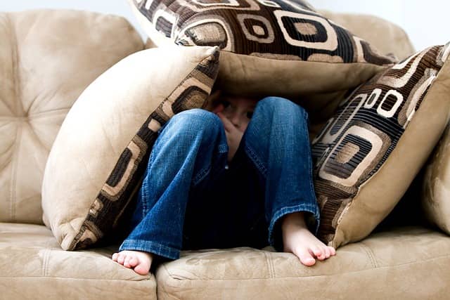 little boy hiding under pillows on couch