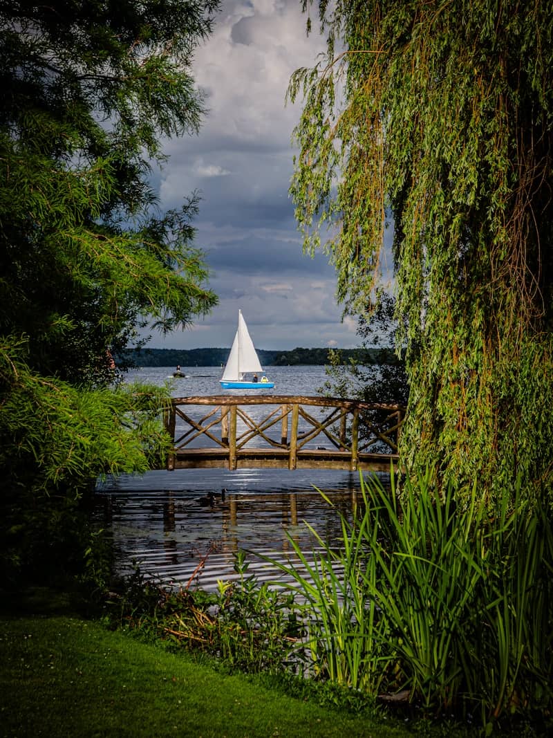 Sailboat on a lake behind a wooden bridge.