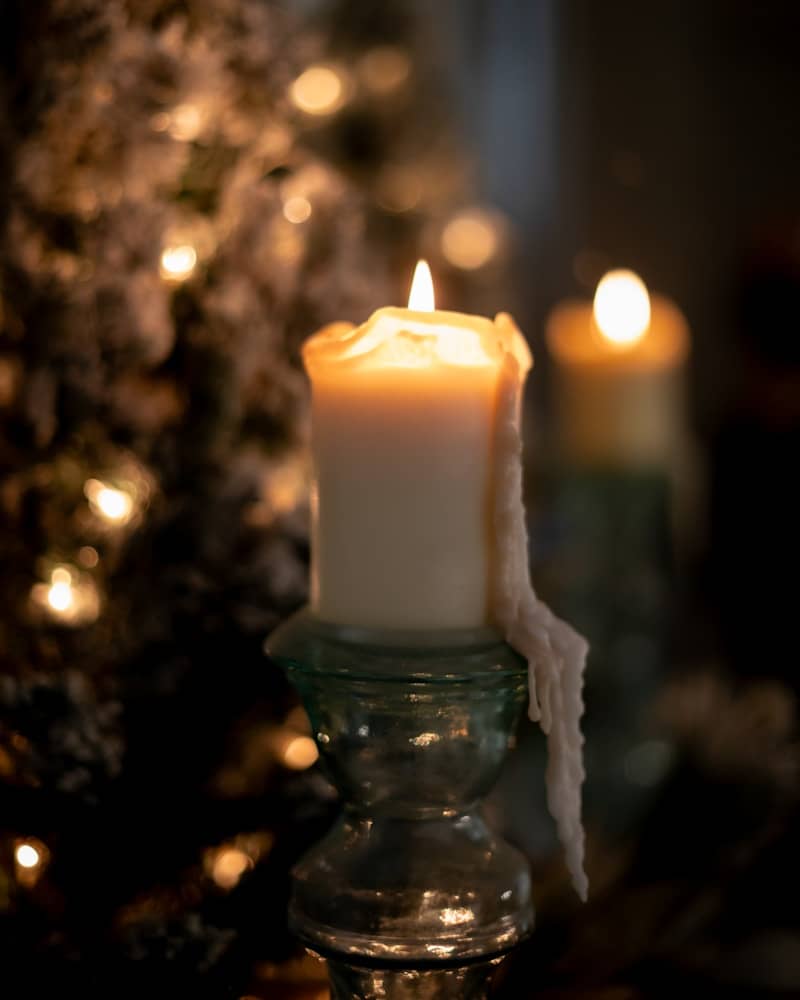 A lit candle with dripping wax, festive lights