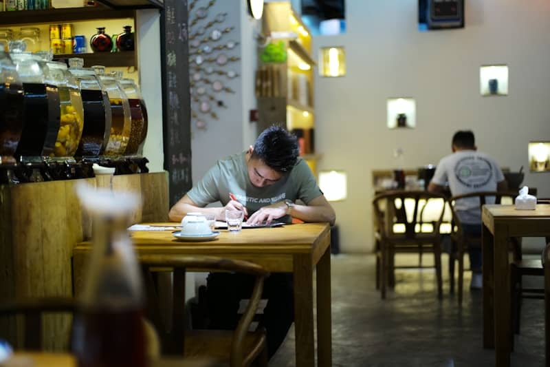 Man writing at a table in a dimly lit cafe.