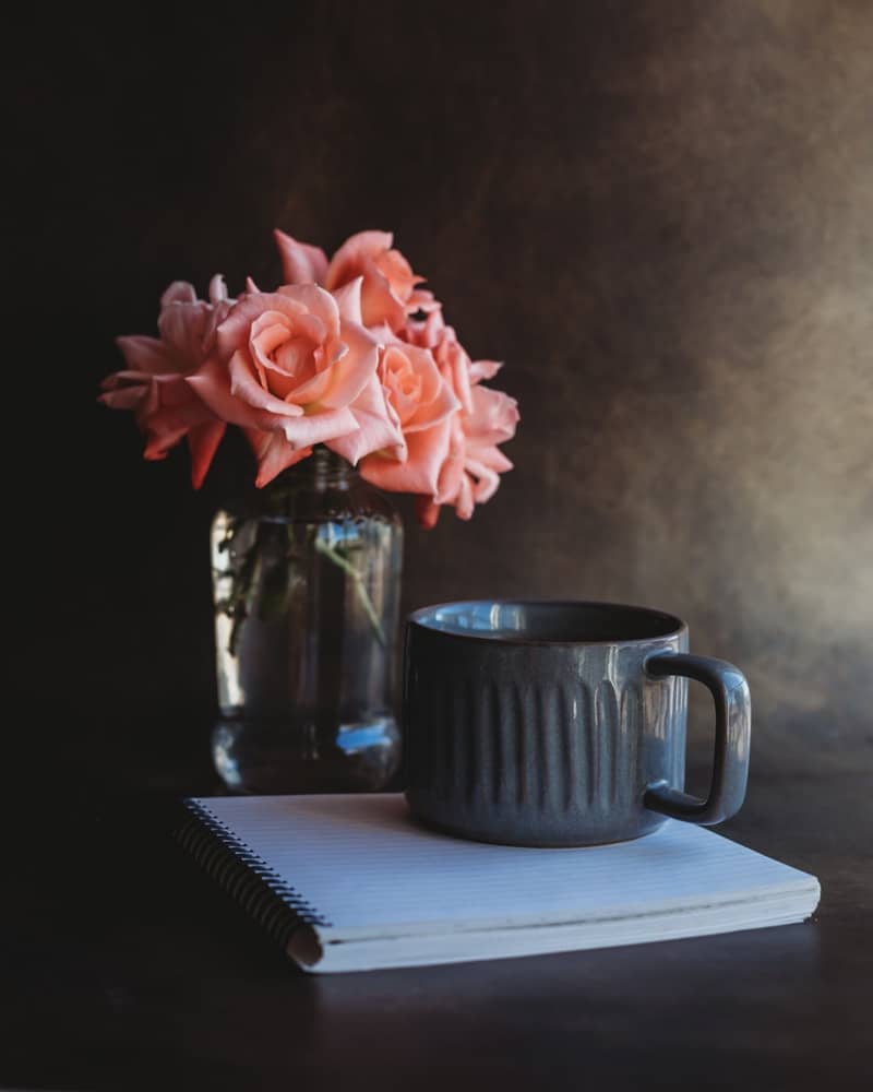Pink roses in a vase next to a mug.