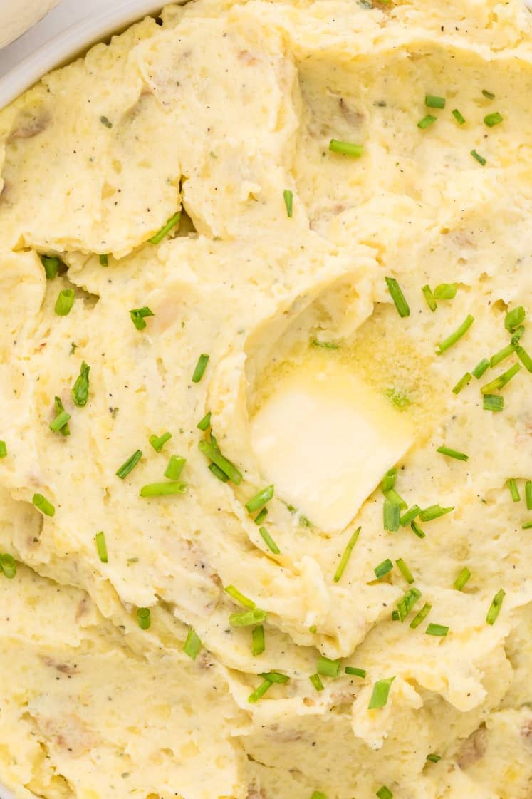 Mashed potatoes topped with chopped chives and a melting pat of butter in the center.