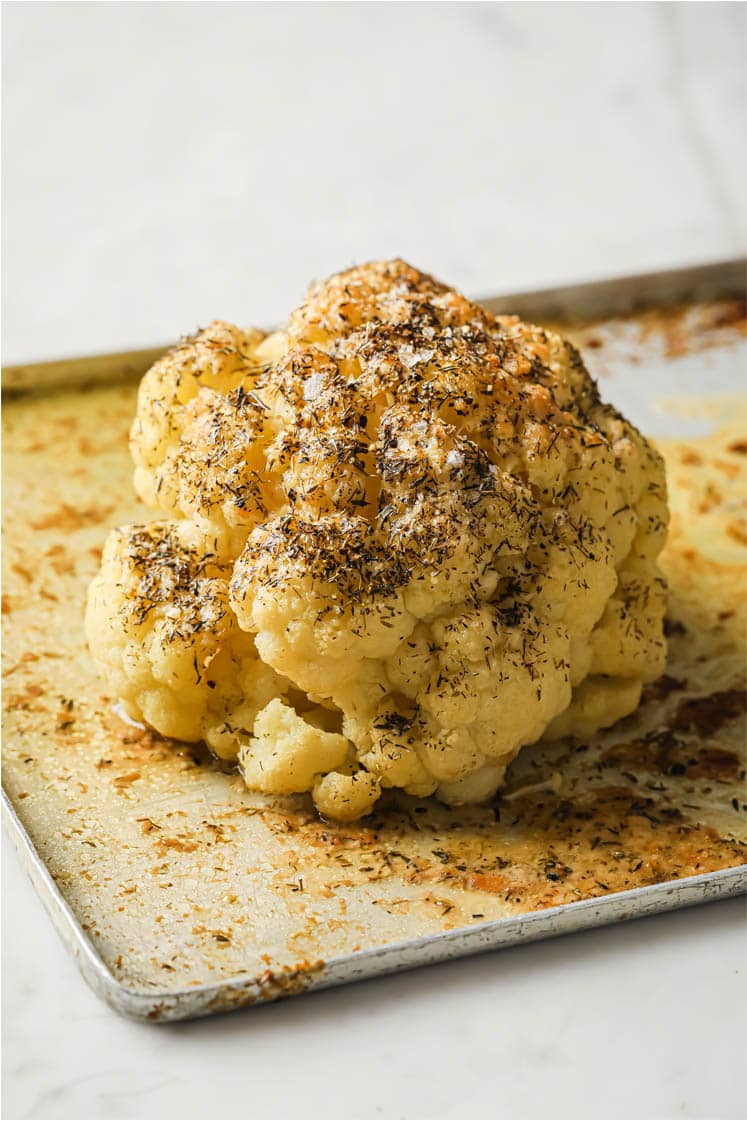 uttery whole roasted cauliflower on a baking sheet.B