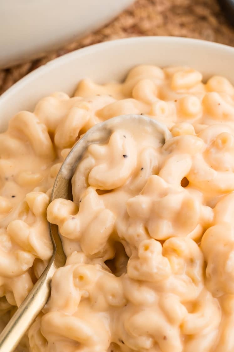 Close-up of creamy macaroni and cheese with a spoon, showing elbow pasta coated in a thick cheese sauce.