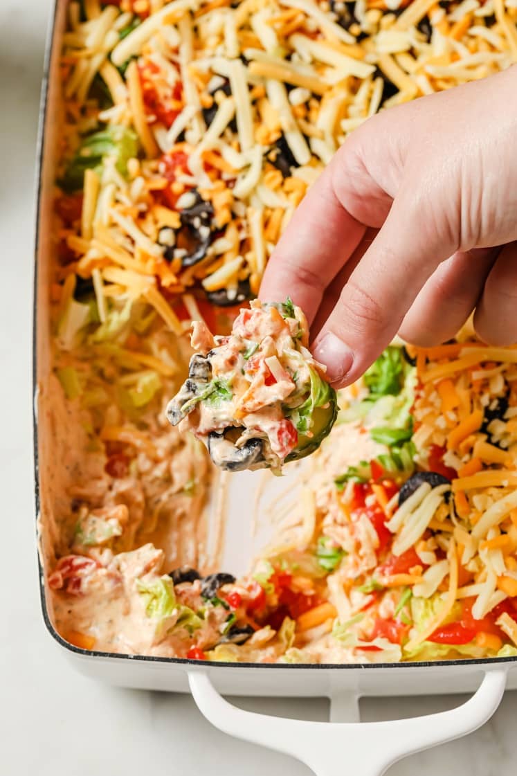 A hand holding a cucumber slice topped with taco dip.