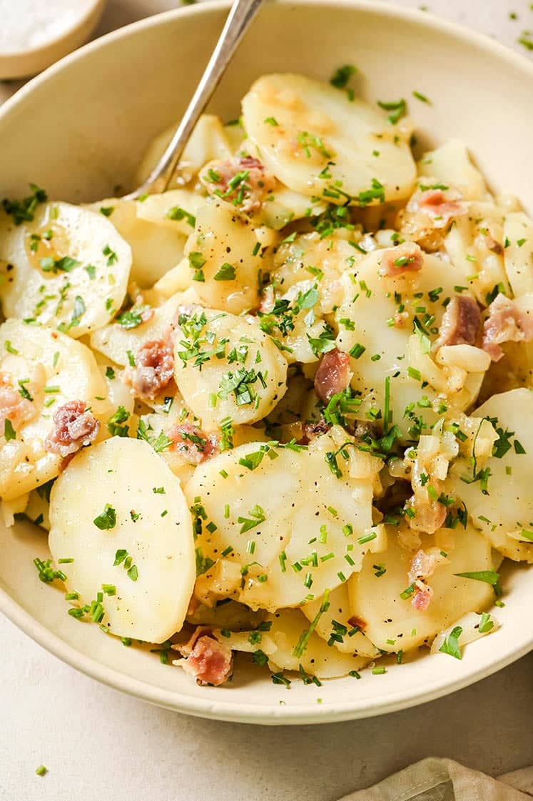 Warm German potato salad with sliced potatoes, crispy bacon, and fresh chopped parsley in a tangy vinegar dressing.
