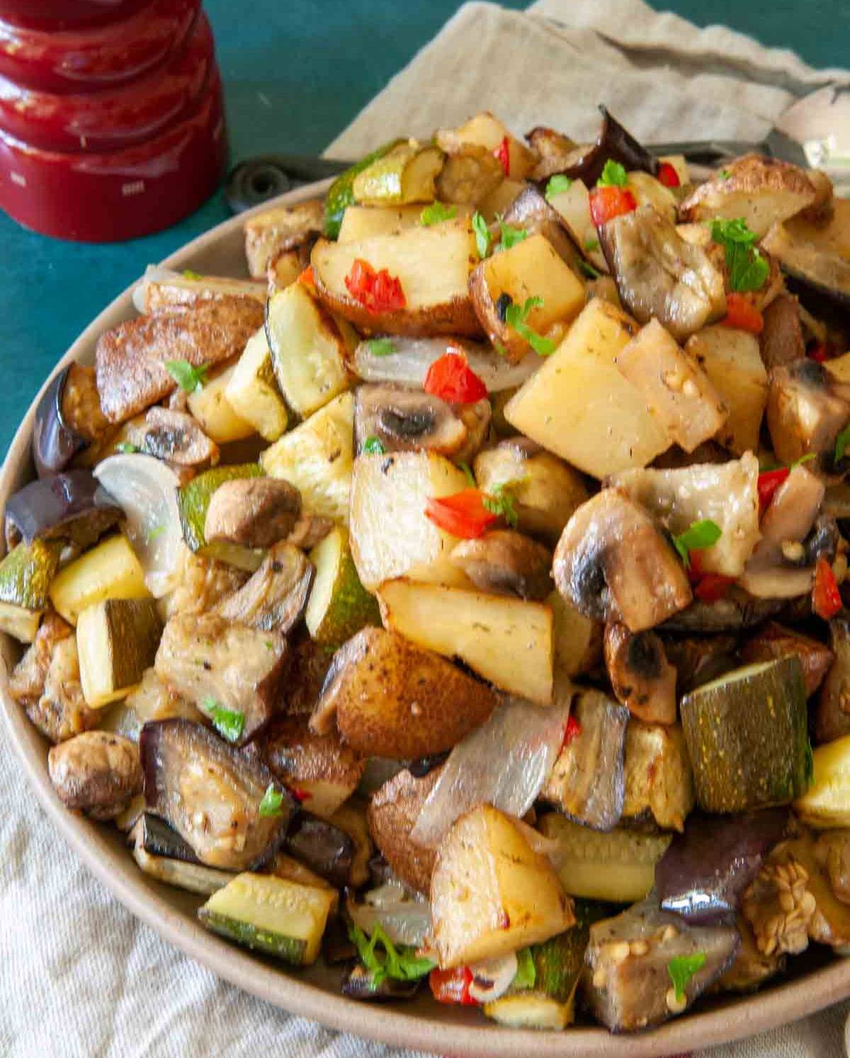 roasted eggplant and potatoes with zucchini and mushrooms garnished with parsley and red peppers