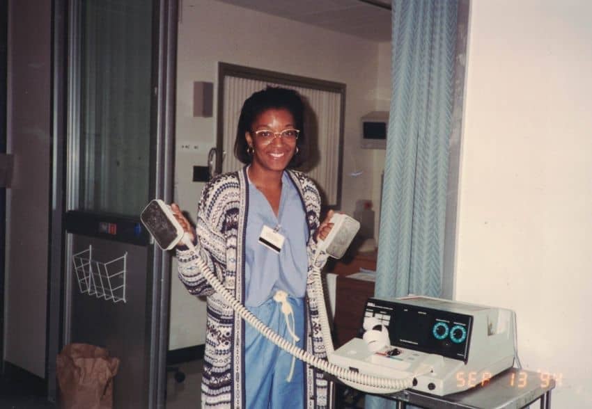 A personal, vintage photograph from September 13, 1994, showing the author as a young healthcare professional in a hospital ICU, wearing blue scrubs and a patterned cardigan while holding defibrillator paddles.