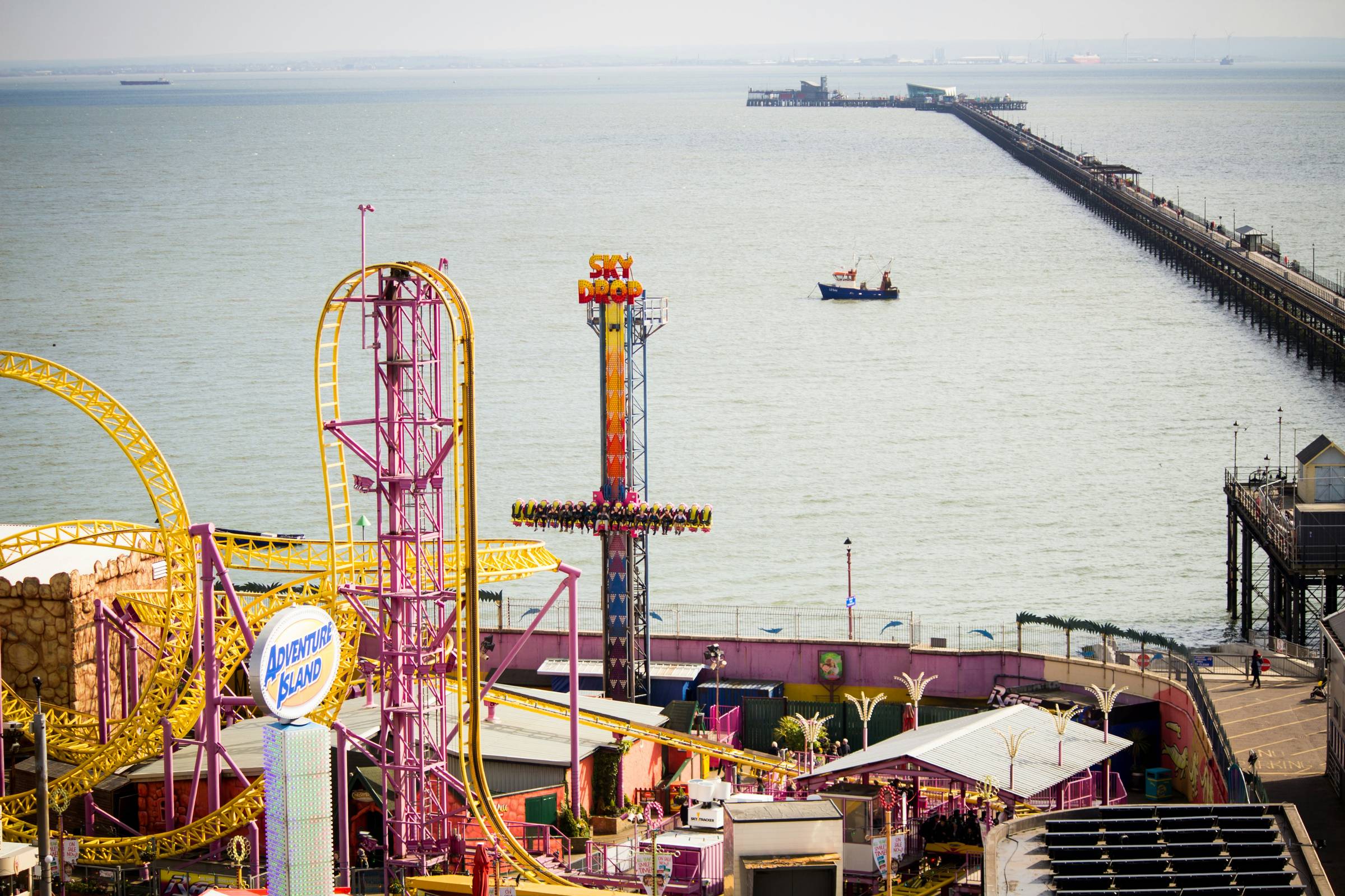 Adventure Island amusement park and Southend Pier on a bright summer day, with colourful rides in the foreground and the long pier stretching out across the sea.