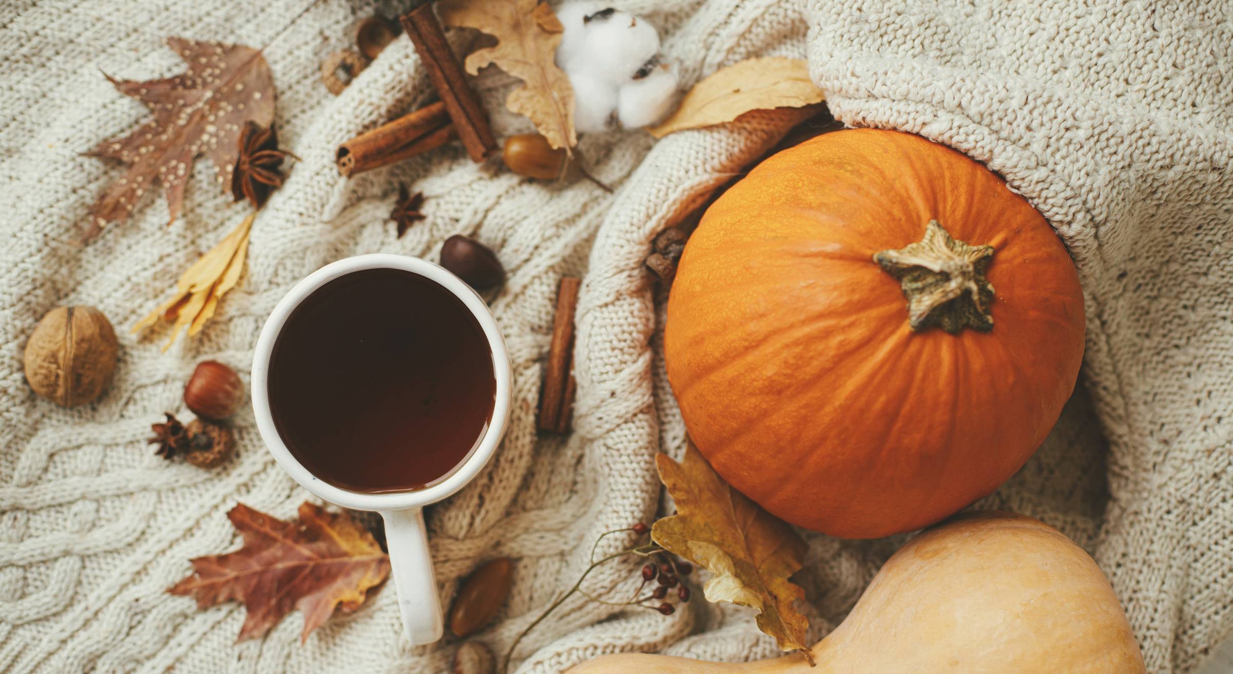 Autumn still life with pumpkin and squash, a mug of hot tea, cinnamon sticks, star anise and fallen leaves on a cream knitted blanket.