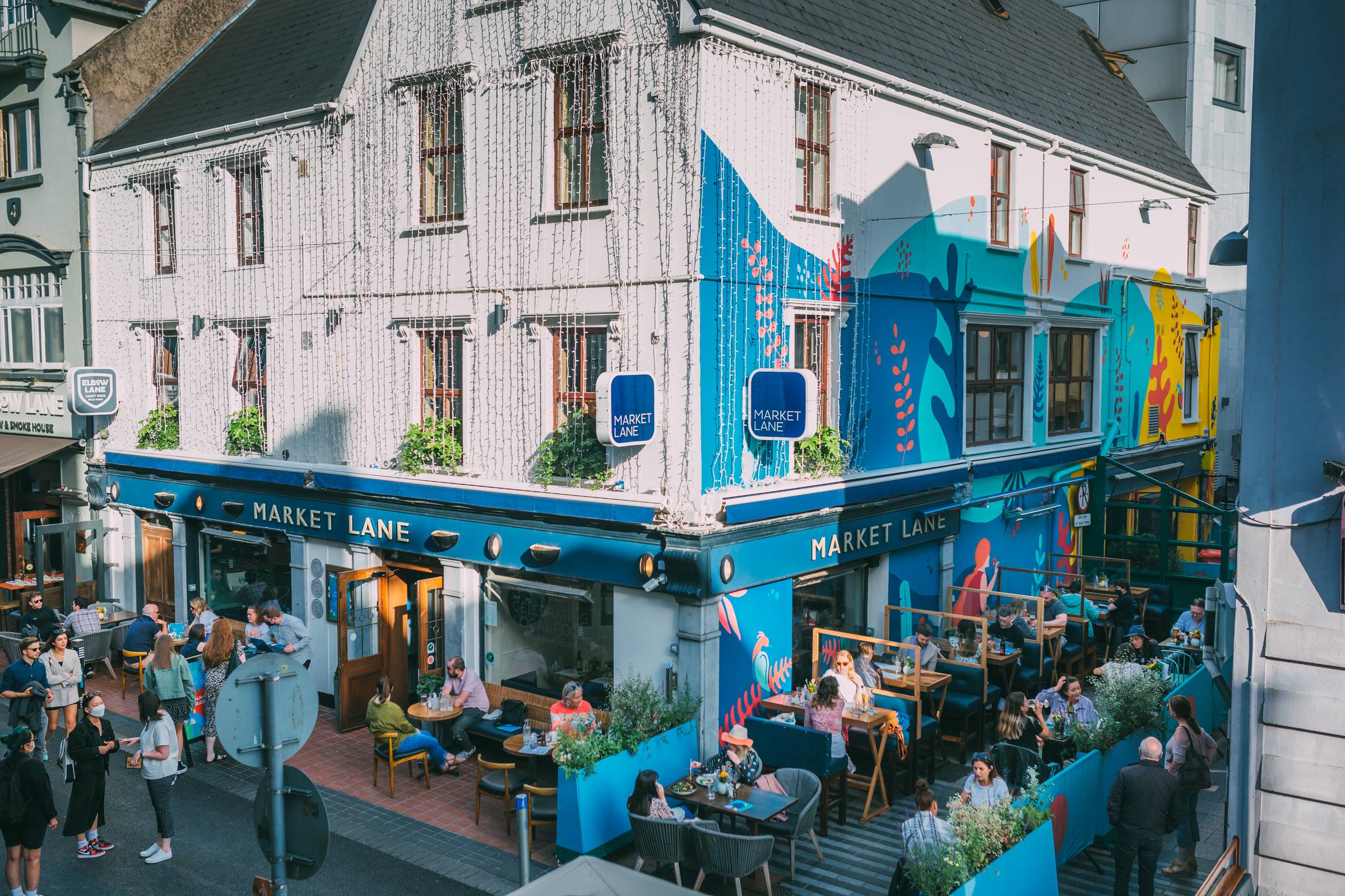 Diners seated outside Market Lane restaurant in Cork city centre, beside its colourful mural.