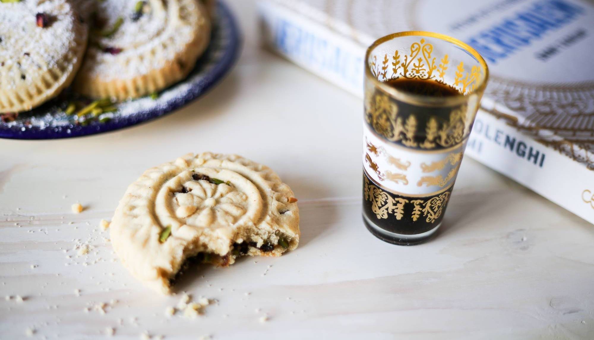 Traditional ma’amoul date cookies, one partially eaten, served with Arabic coffee on a white table