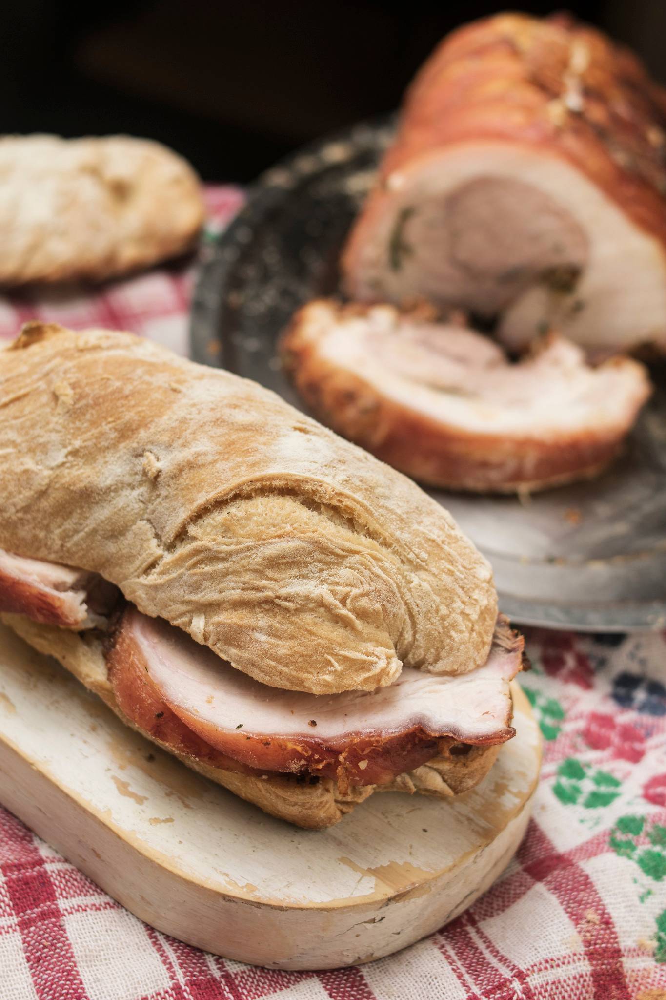 Ciabatta roll filled with thick slices of porchetta, with the remaining roast and carved slices in the background.