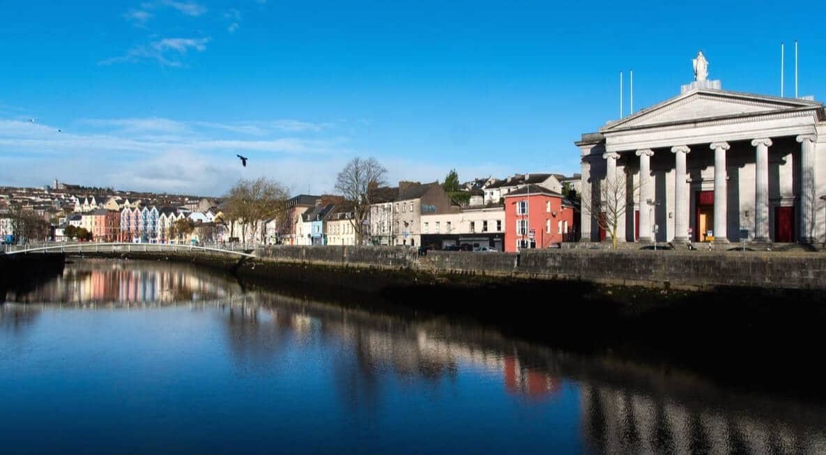 River Lee reflecting the colourful buildings of Pope’s Quay and St Mary’s Priory in Cork beneath a clear blue sky.