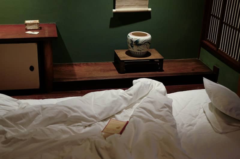 An undone bed in a dark, green room.