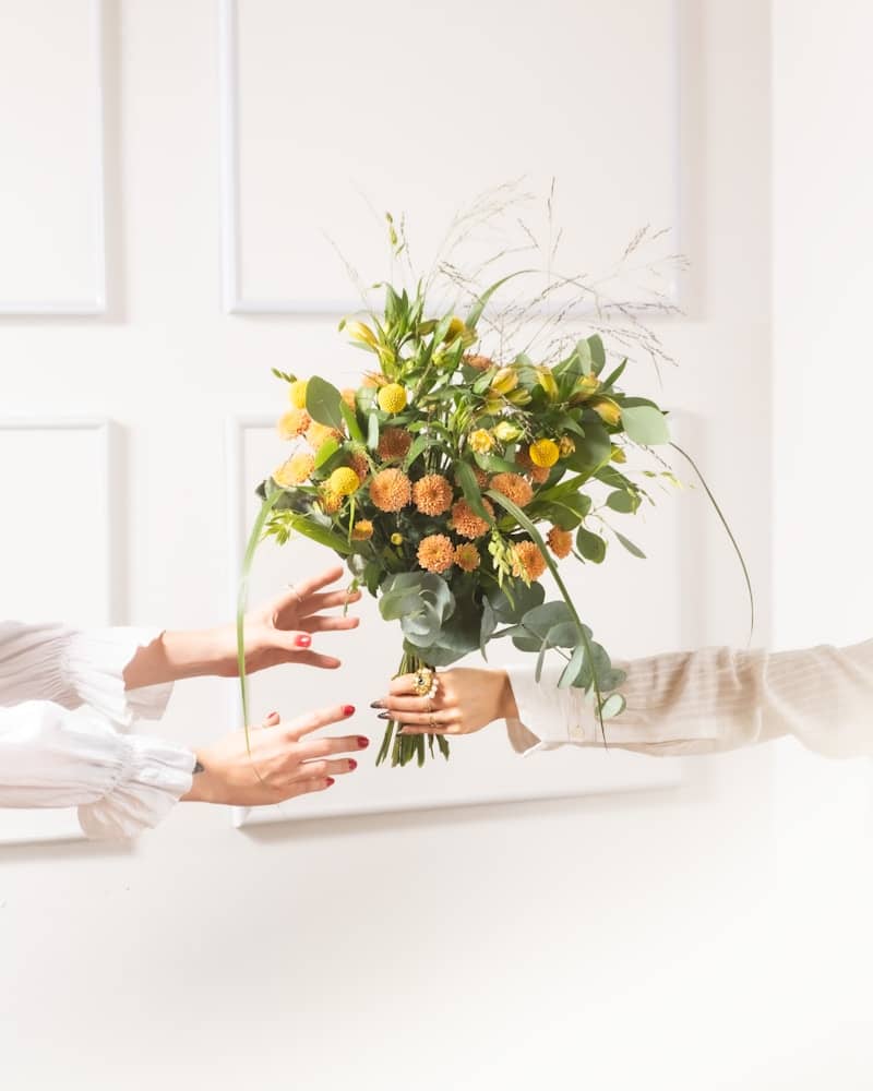 Hands exchanging a bouquet of yellow and orange flowers.