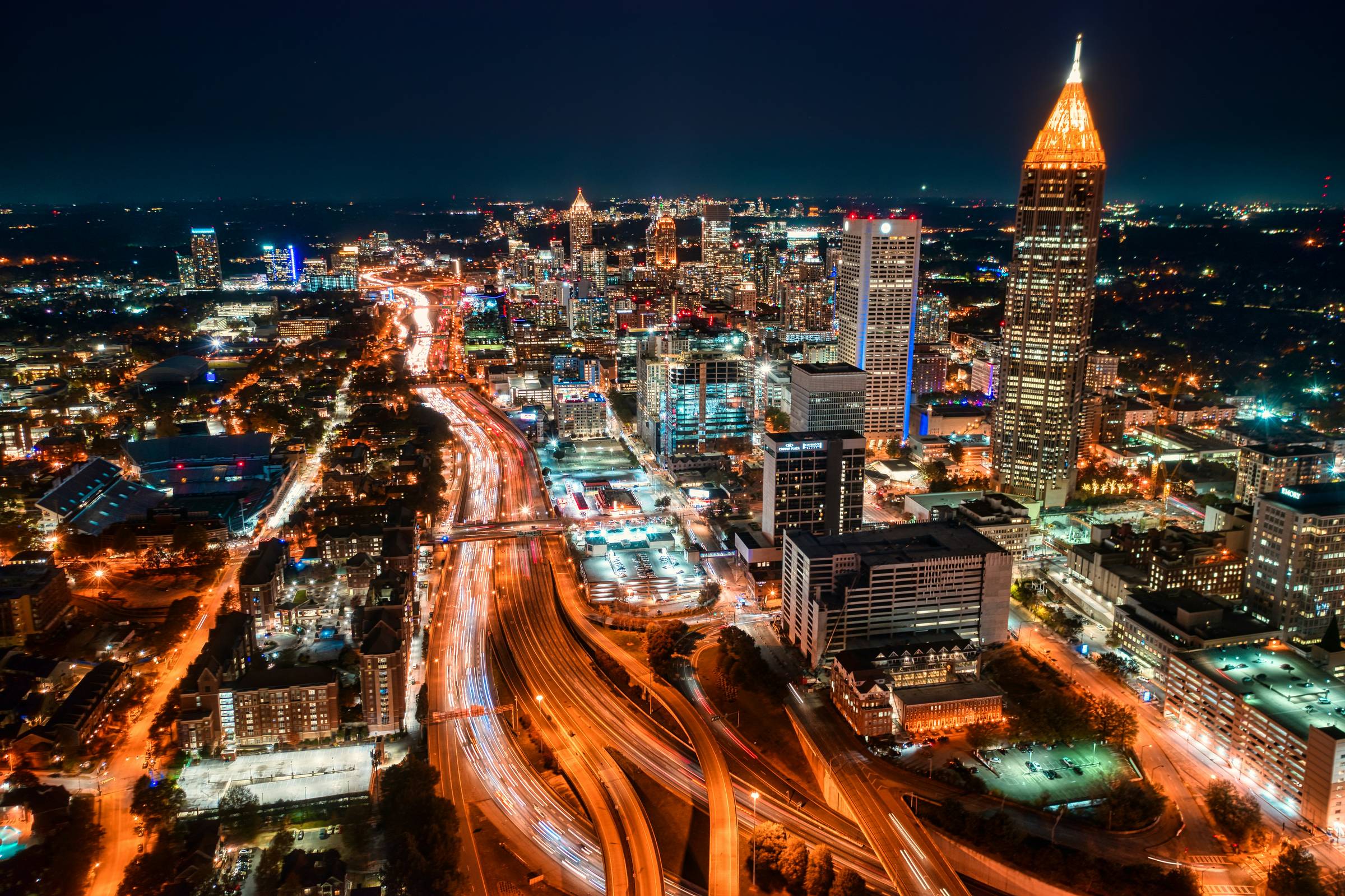 Image of various buildings in Atlanta and a highway taken at night with the roads and building lights on.