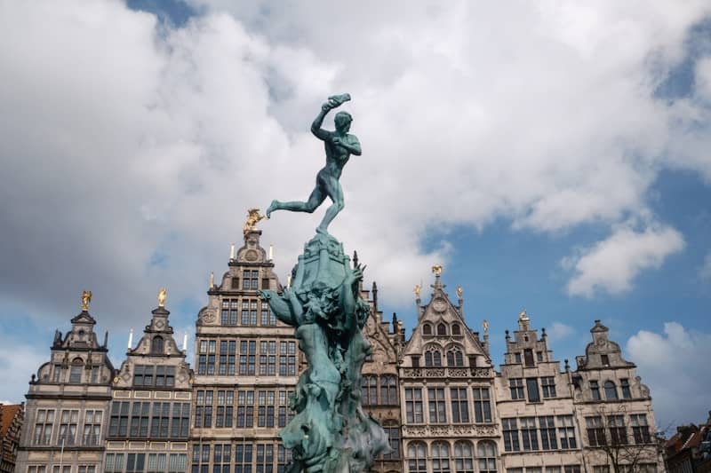 A bronze statue stands atop a fountain with buildings behind.