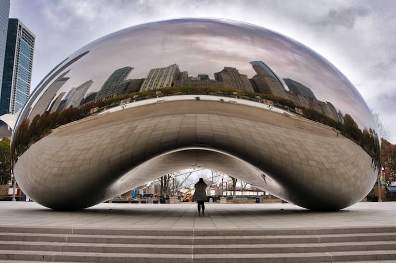Cloud gate sculpture reflecting city skyline and a person