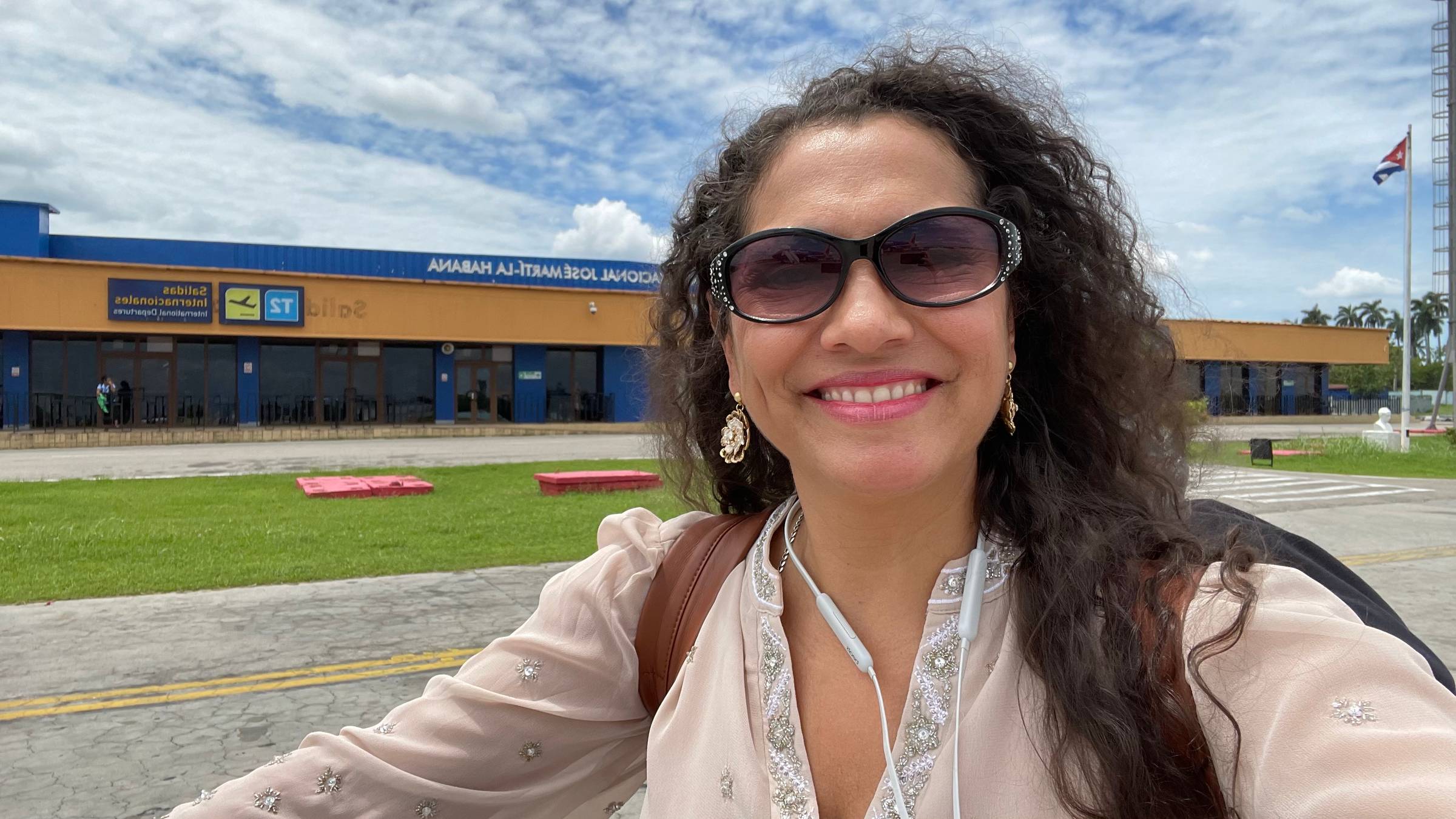 Sheyla Paz standing at José Martí International Airport in Havana, Cuba, during her arrival with luggage and supplies for her journey.