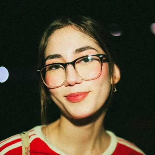 A woman wearing glasses and a red striped shirt against a dark bokeh background