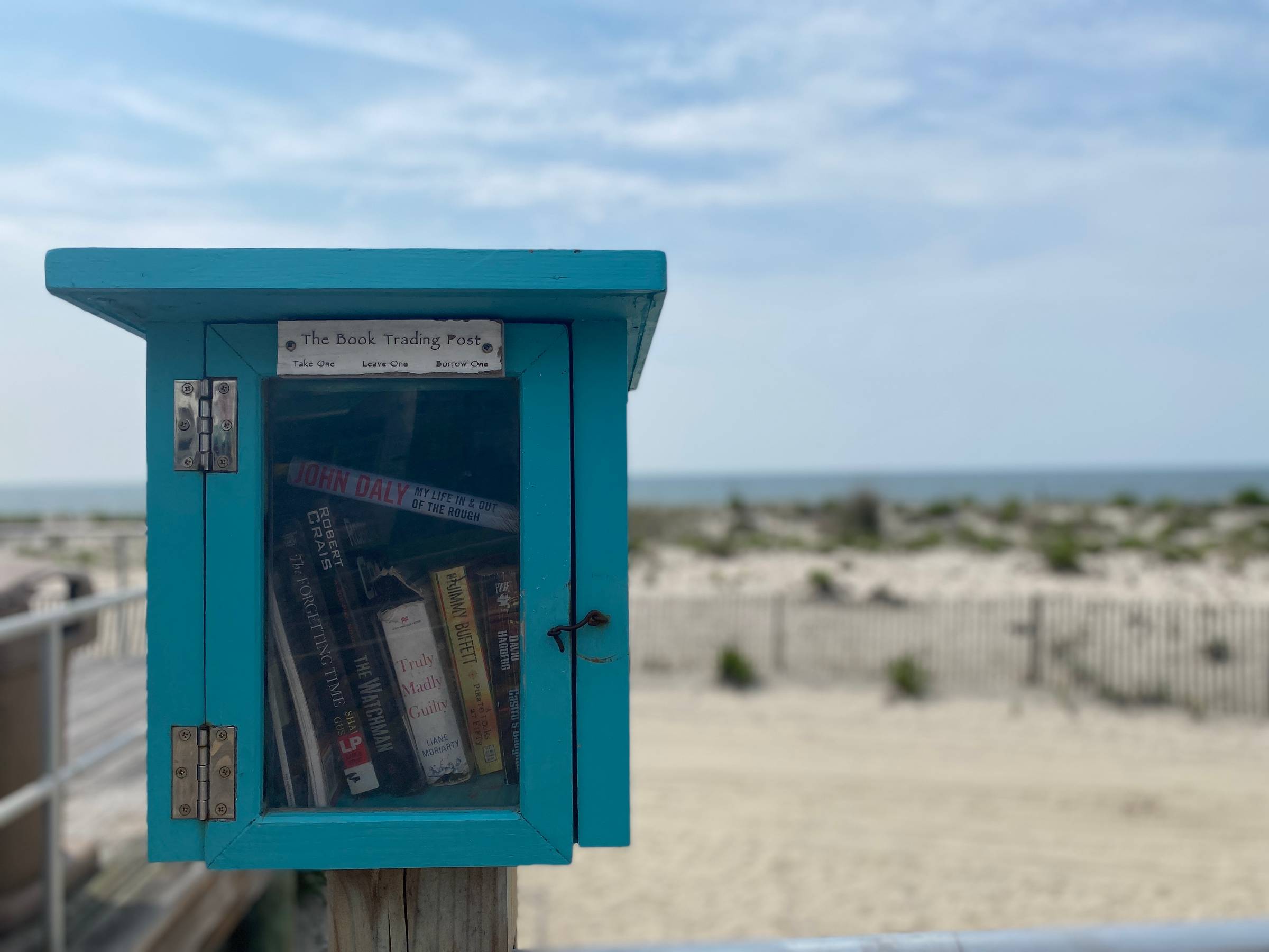 A little free library is in the foreground, and the beach and ocean are in the background