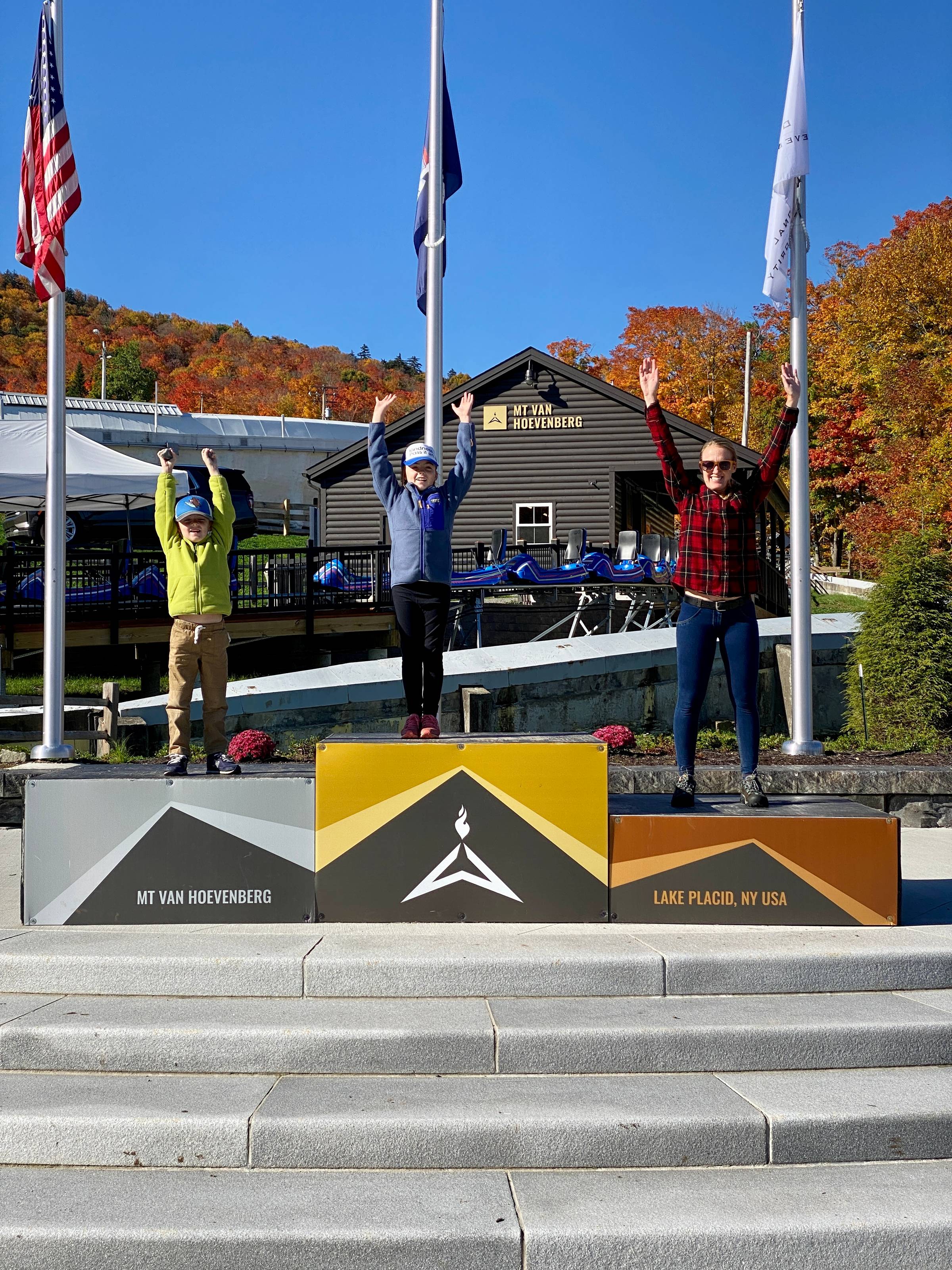 3 people stand on the Olympic winners podium at the Olympic Jumping Complex