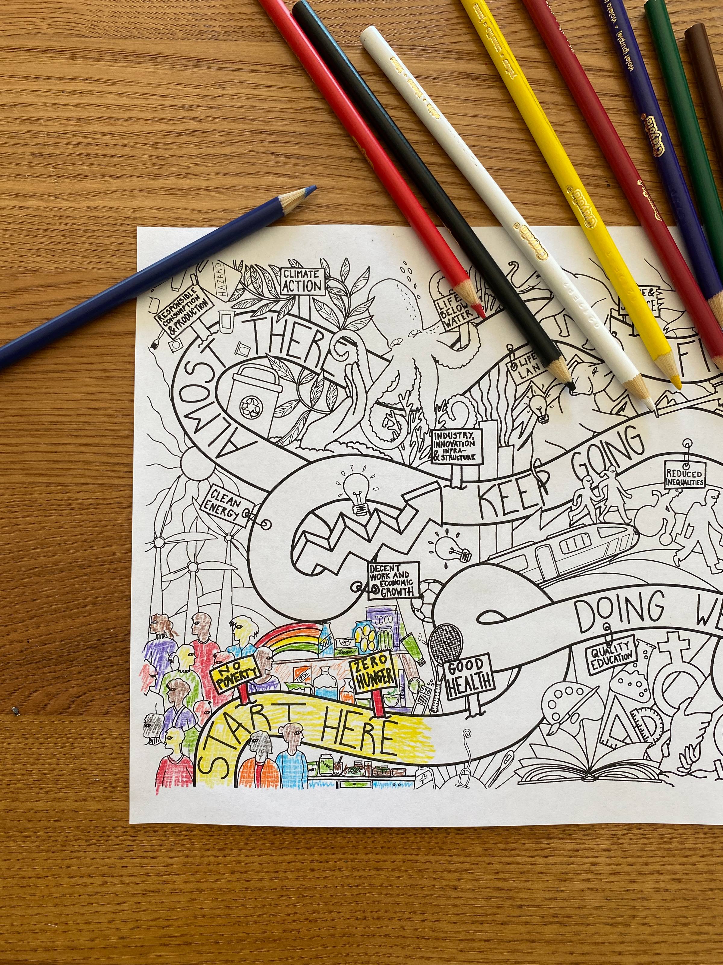 The sustainable development goals coloring poster sits on a wooden table with colored pencils above it.