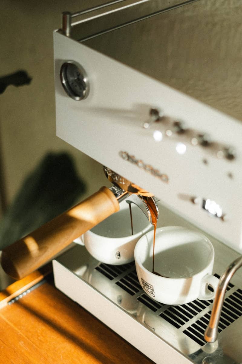 Coffee is brewing in two white cups.