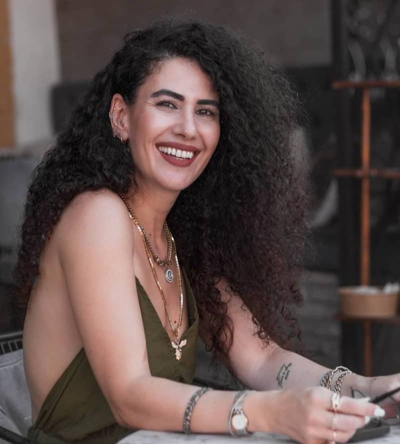 A smiling woman with curly hair wearing jewelry