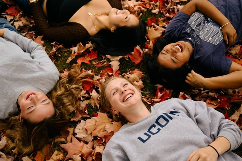 Four friends laughing while lying on autumn leaves
