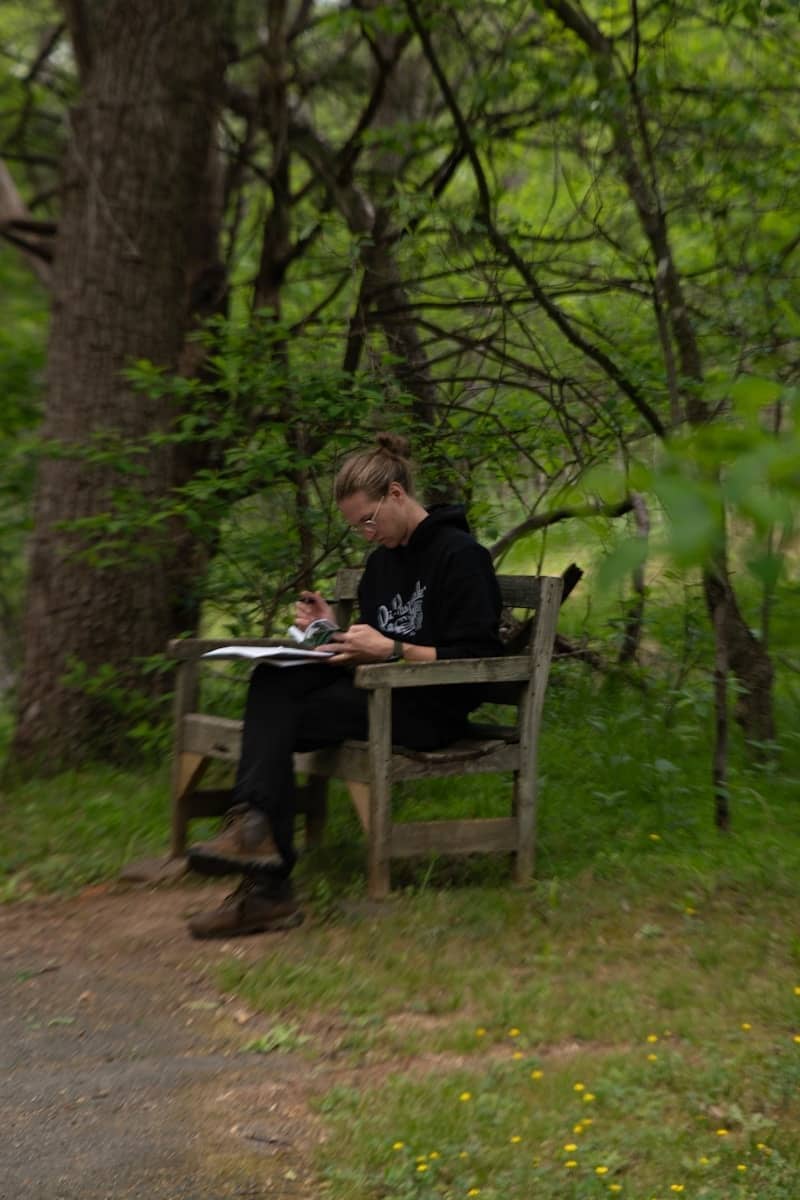 A person sketching on a wooden bench in a forest.