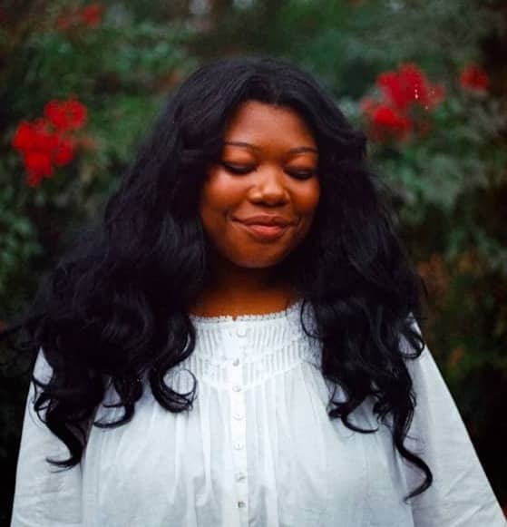 A woman with long, dark, curly hair smiles.