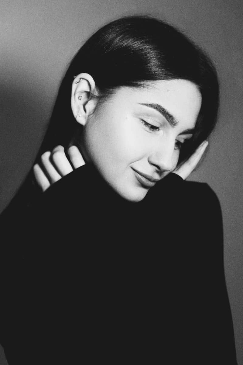 A woman with dark hair in a black turtleneck sweater against a grey background