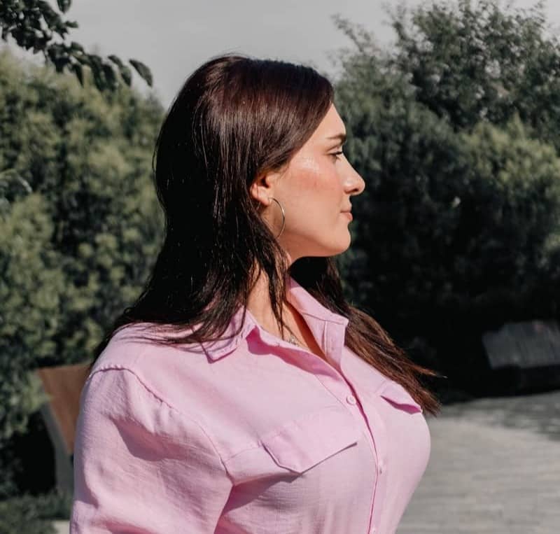 A woman in a pink button-down shirt and white skirt in a park