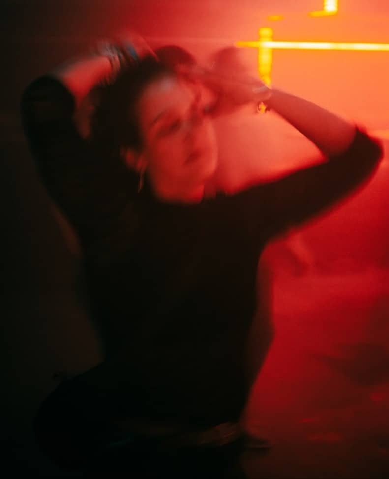 Blurred woman dancing under vibrant red and orange lights.