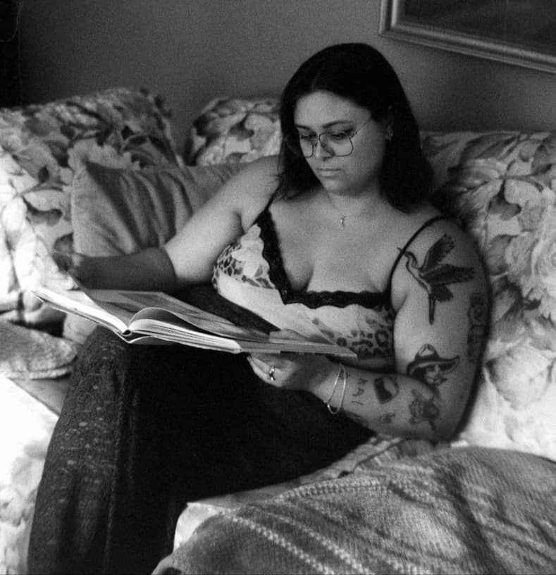 Woman with tattoos reading book on couch