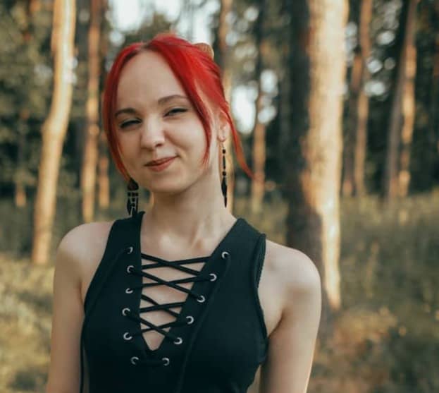 Young woman with red hair in a black dress outdoors.