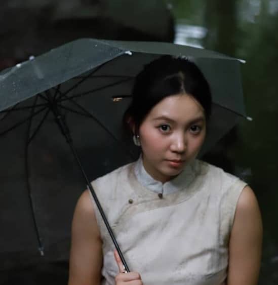 A woman holds an umbrella under green leaves near water.