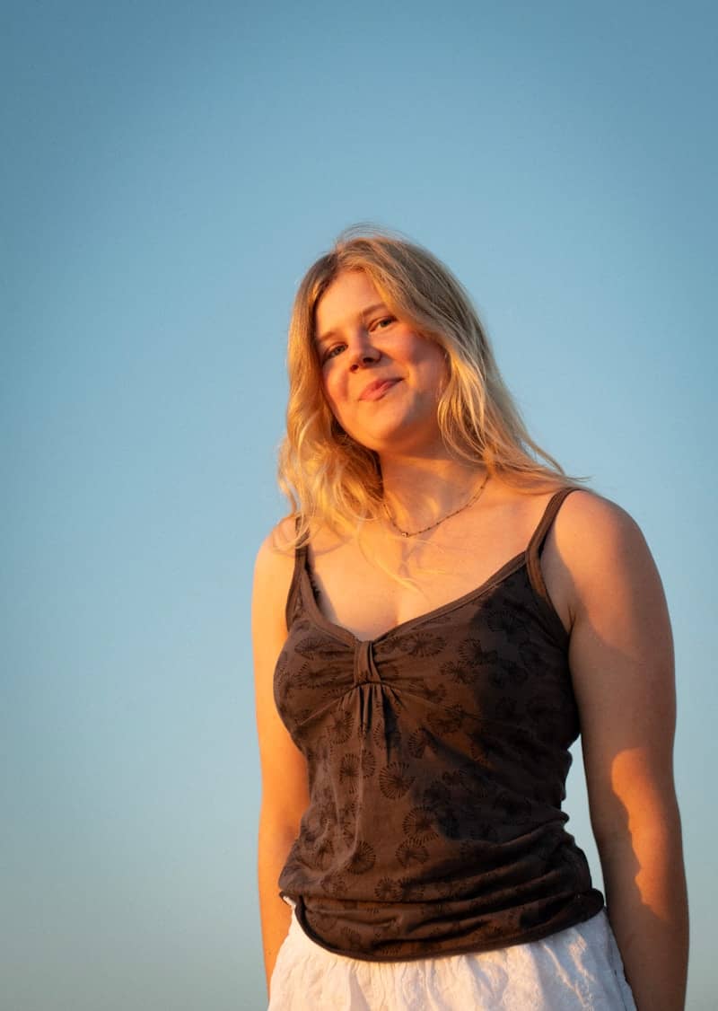 A young woman smiles against a clear sky.