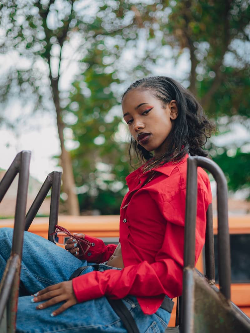 Young woman in red shirt and jeans sits outdoors.