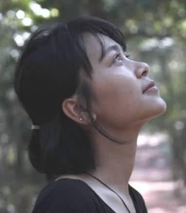 Woman gazes upwards amidst the trees, serene and thoughtful.