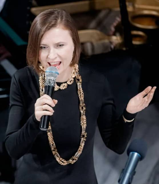 A woman in a black dress singing into a microphone on a stage