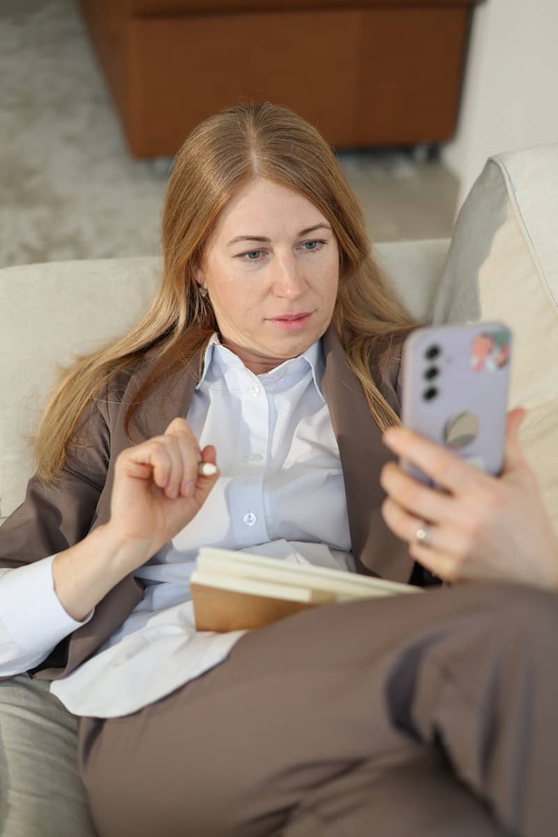 Woman looking at phone while holding a pen and notebook.