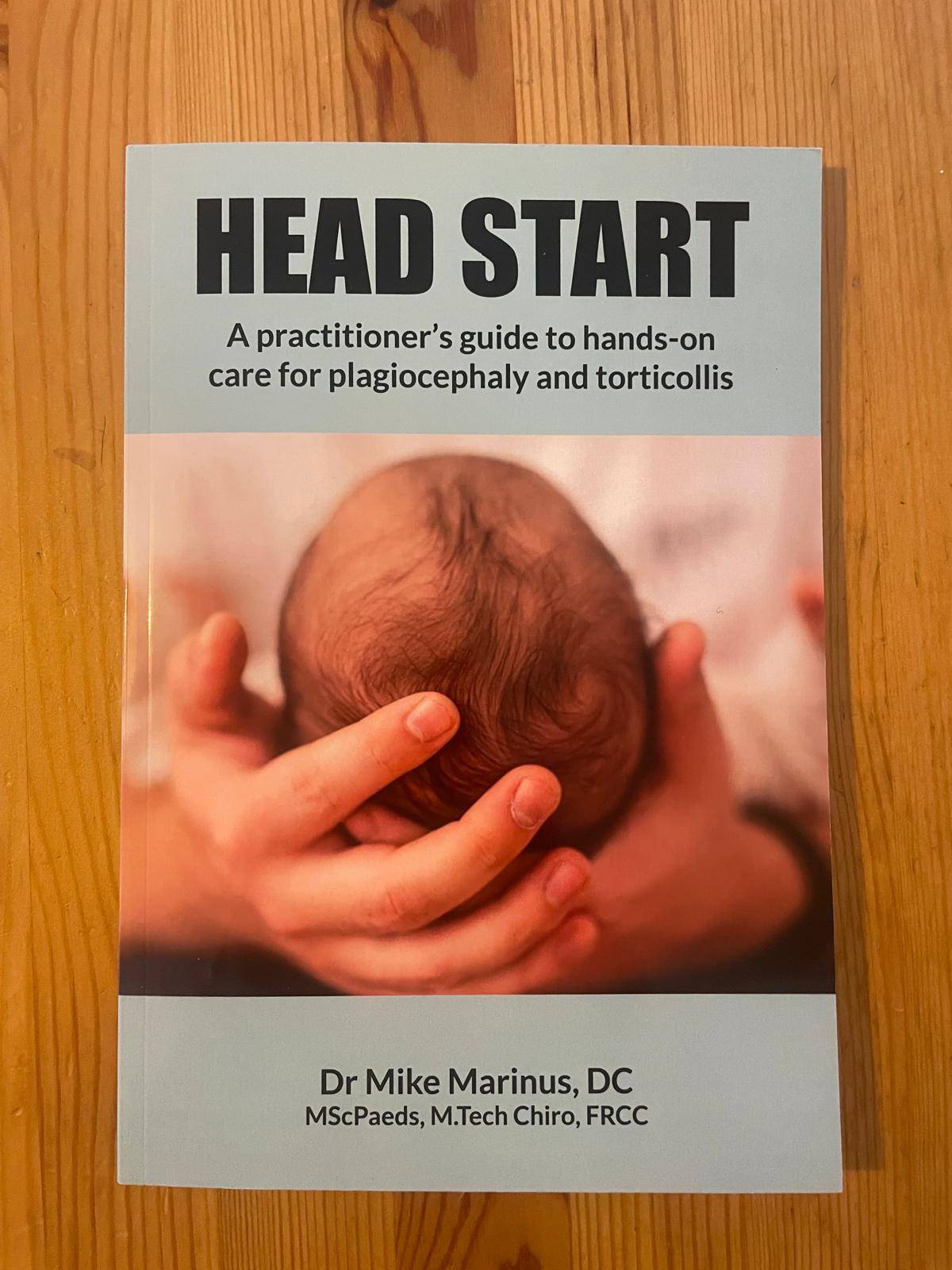 Textbook called: A practitioners guide to hands-on care for plagiocephaly and torticollis. Image has a man's hand holding a baby's head.