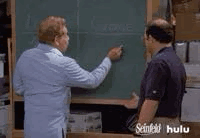 Man showing another man that he is drawing a circle with chalk on a classroom board