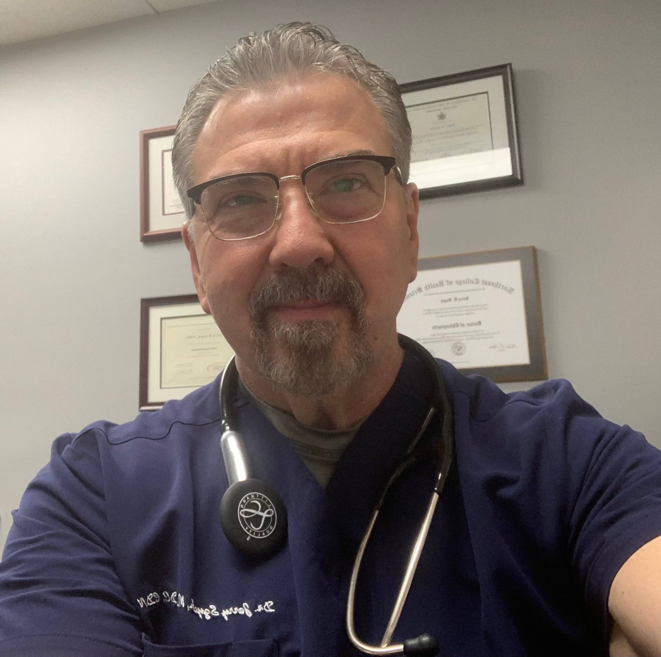 Jerry Szych, Nurse Practitioner, smiles in a selfie while wearing his scrubs.