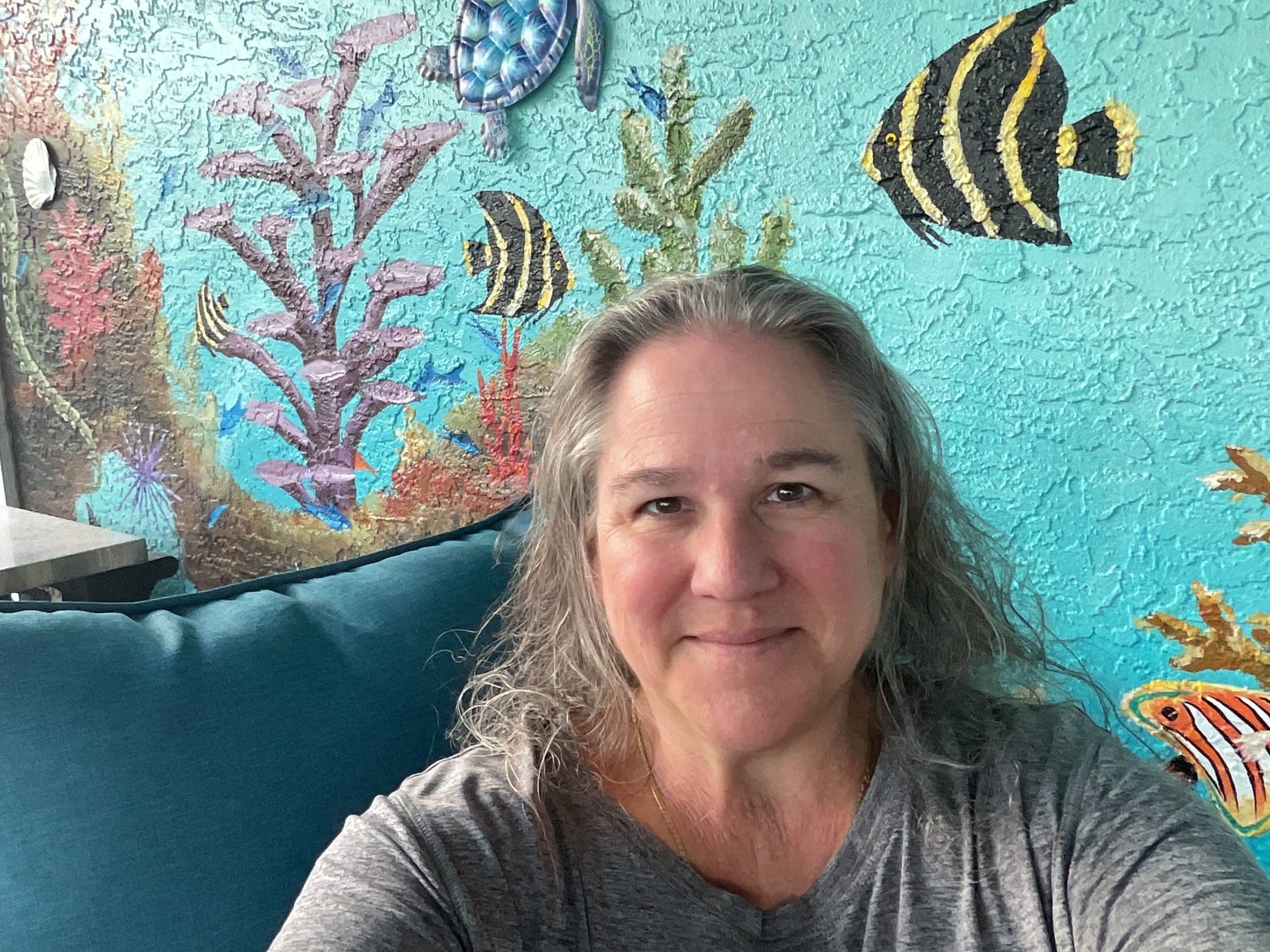 Smiling nurse standing outdoors in front of a colorful backyard mural featuring fish and other sea life.