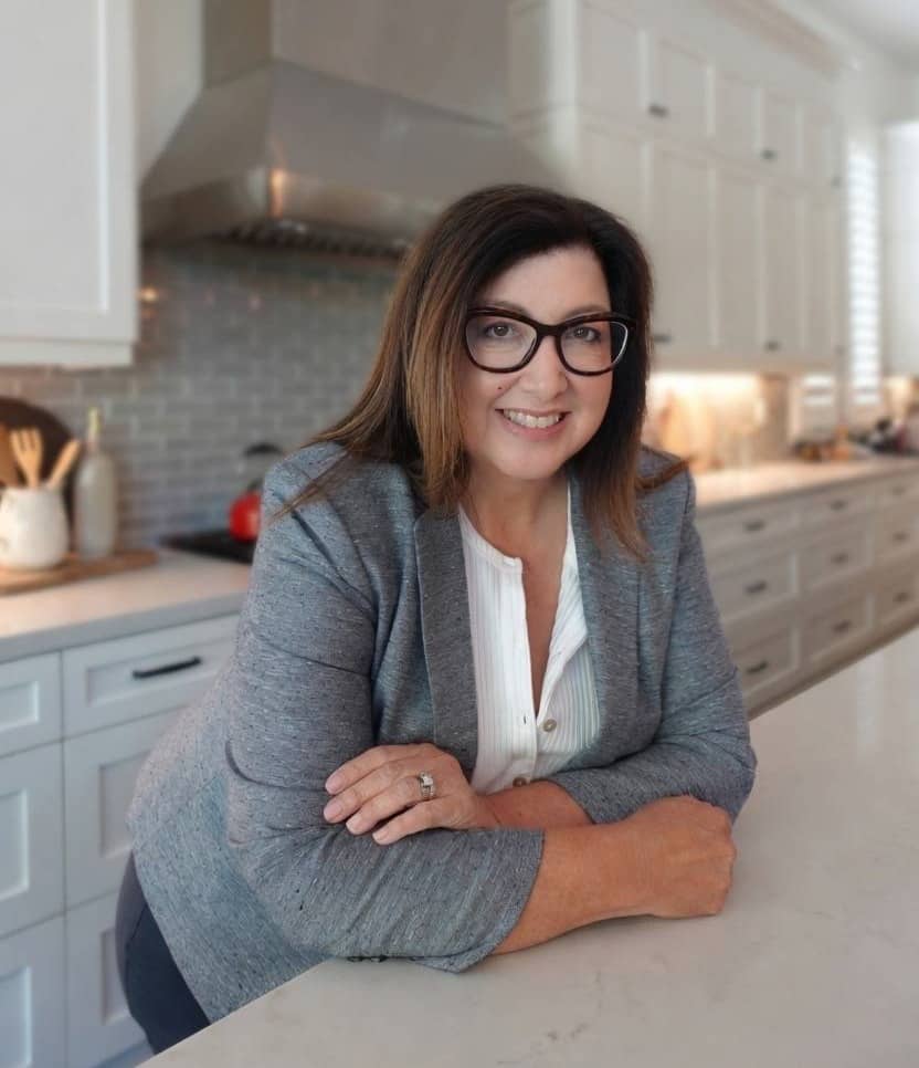 Rebecca Sanchez-Emery, MSN, RN, PHN, smiling while leaning on a kitchen counter.